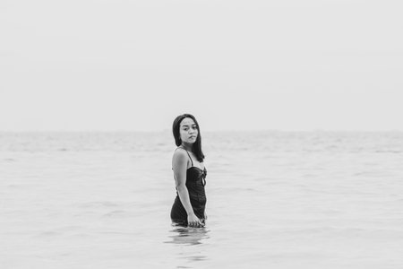 Minimalist monochrome image of a woman immersed waist-deep in the sea, conveying solitude,...