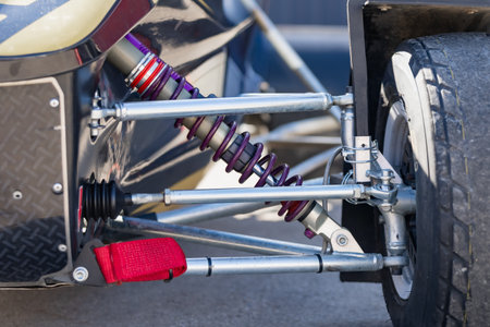 Motorsport buggy chassis detail with coilover suspension, metal wishbones, steering rod, axle joint, wheel and protective panel