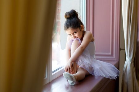 Little girl ballerina in white tutu sitting on floor in ballet class.の写真素材