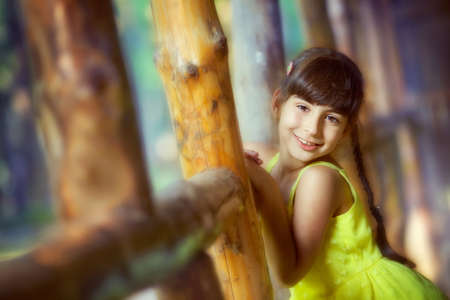 A child girl in a bright yellow dress stands by a log buildingの写真素材