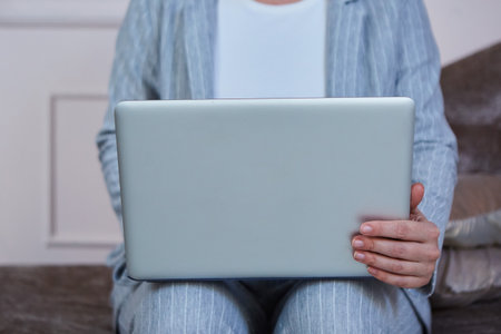 The laptop is lying on the lap of a girl in office clothes, who is sitting on the sofa. close-up. Photo inside the room.の写真素材