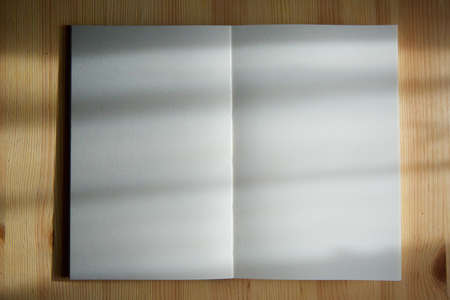 An open notebook with blank pages lies on the wooden surface of the table in the rays of side light.の写真素材