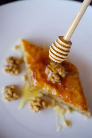 Close-up - hand of an unidentified cook is pouring - a piece of cake with a walnut - honey from a wooden spoon. Confectionery conceptの写真素材