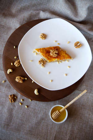 Close-up dessert is a piece of cake with walnuts, honey and pine nuts. The food is on the table with a linen tablecloth. Concept of confectioneryの写真素材