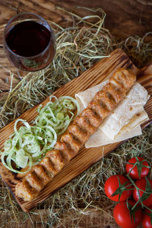 Pieces of roasted kebab meat on pita bread are served with fresh tomatoes and onions on hot pepper and a salad on a wooden Board and hay. Restaurant dish from the chef.の写真素材