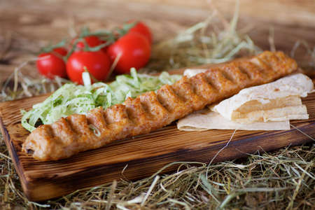 Pieces of roasted kebab meat on pita bread are served with fresh tomatoes and onions on hot pepper and a salad on a wooden Board and hay. Restaurant dish from the chef.の写真素材