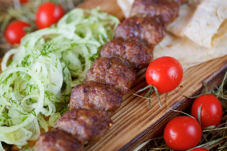 Pieces of roasted kebab meat on pita bread are served with fresh tomatoes and onions on hot pepper and a salad on a wooden Board and hay. Restaurant dish from the chef.の写真素材