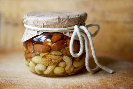 Jam of different types of nuts in syrup or honey in a glass jar on the table.