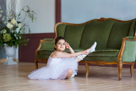 Little girl ballerina in white tutu sitting on floor in ballet class.の写真素材
