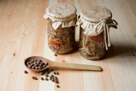 Two cans of pickled mushrooms are standing on the wooden surface of the table. Next are spices.