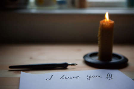 The inscription I love you in the form of a letter by hand with a pen on white paper and a candle...