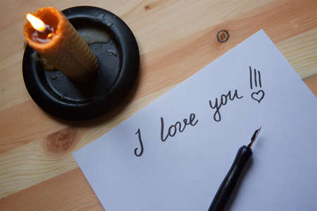 The inscription "I love you" in the form of a letter by hand with a pen on white paper and a candle burning on the table. love letter.の写真素材