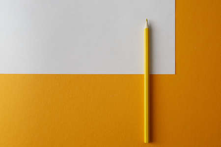 Yellow colored pencil lying on a bright yellow and white background, macro photography.