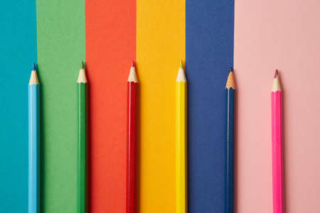 Several colored pencils of various shades lie on a bright colored background of various shades, each...