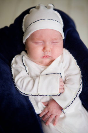 Little newborn baby boy lying in white clothes on dark background.