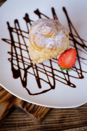 Cake eclairs lie on a white plate on chocolate gravy. The product is sprinkled with white powdered...