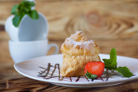Cake eclairs lie on a white plate on chocolate gravy. The product is sprinkled with white powdered...