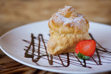 Cake eclairs lie on a white plate on chocolate gravy. The product is sprinkled with white powdered...