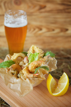 Shrimp, squid rings and other seafood deep-fried in batter and a glass of beer. A beer snack and a light snack.の写真素材