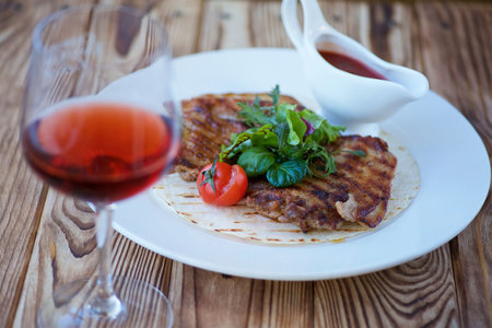 A piece of fried meat lies on a white plate. Decorated with vegetables and herbs. There is a red sauce nearby. The concept of recipes from the restaurant and dishes from the chef.の写真素材