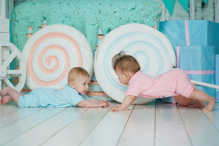 A two baby lies on a soft surface in a bright room, dressed in blue and pink clothing. The concept of childhood and baby care.の写真素材