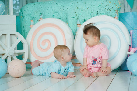 A two baby lies on a soft surface in a bright room, dressed in blue and pink clothing. The concept of childhood and baby care.の写真素材