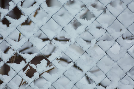 Old iron fence netting covered with snow in winter in the villageの写真素材