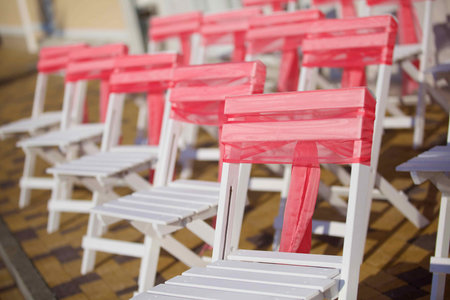 Chairs standing in a row and decorated with red ribbon for the wedding ceremony.