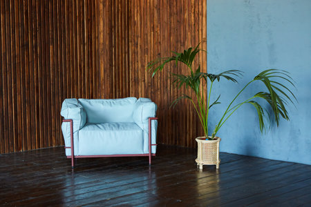 A white armchair stands against a wooden wall. Next to a plant. Loft-style interior design.の写真素材