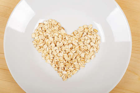 Oat flakes on a white plate in the form of a heart on a wooden background top viewの写真素材