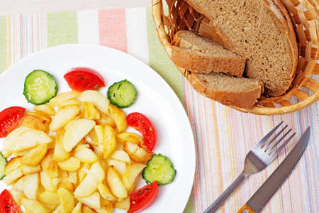 Fried potatoes on a plate of bread cucumbers tomatoesの写真素材