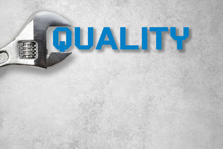 Wrench holds lettering quality in front of a gray concrete wallの写真素材