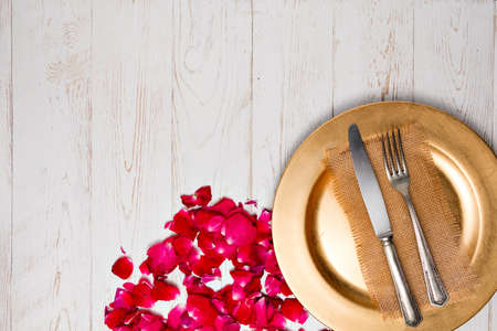 Cutlery on a napkin lying on an old white Decorated with rose petals wooden table
