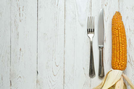 Cutlery on old rustic wooden table with corn on the cob (Zea mays)の写真素材