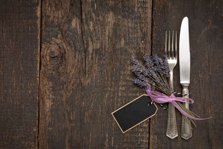 Cutlery lying on an old wooden table with lavender bouquetの写真素材