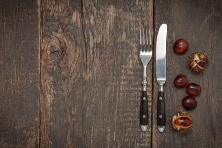 Cutlery and chestnuts lie on a rustic old wooden tableの写真素材