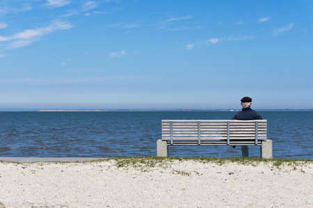 Old sailor sitting on a bench looking out at sea