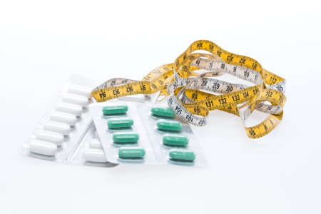 Tape measure and pills on a white tableの写真素材