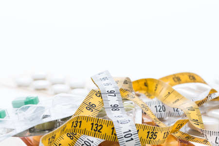 Tape measure and pills on a white tableの写真素材