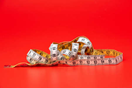 Yellow white tailor tape measure to take measurements and measure, red backgroundの写真素材