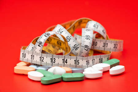 Tape measure and pills on a red background