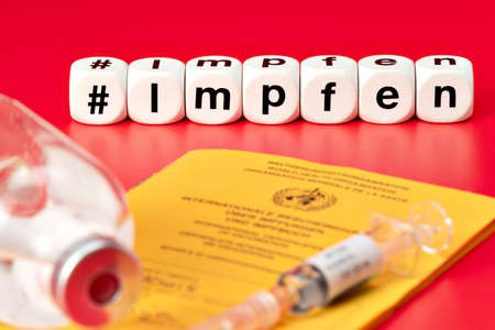 Syringe with vaccine and International Vaccination Passport. Vaccination written with dice. (Impfen...