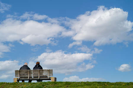 Mature couple sitting on a bench and looking into the distanceの写真素材