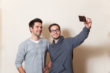 Two smiling men are doing a self portrait with a cellphoneの写真素材