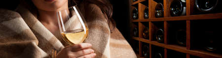 Glass of wine in woman's hands on wooden wine rack backgroundの写真素材