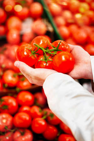Man holding a bunch of fresh tomatoes on the background of shelved red tomatoes