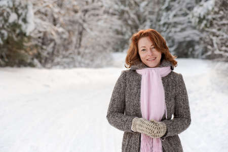 Smiling red-haired woman having fun on winters day in forest.の写真素材