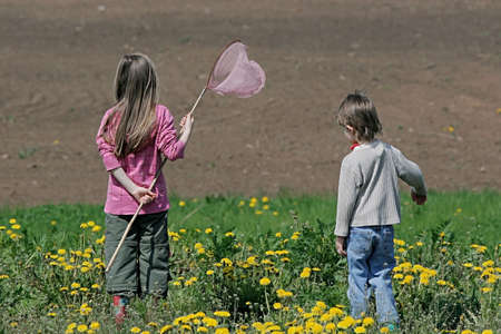 Brother and sister enjoy summer time in the dandelion meadow.の写真素材