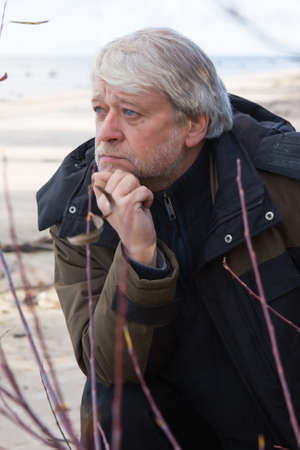 Portrait of mature thoughtful man with grey hair at the Baltic sea in autumn day.の写真素材
