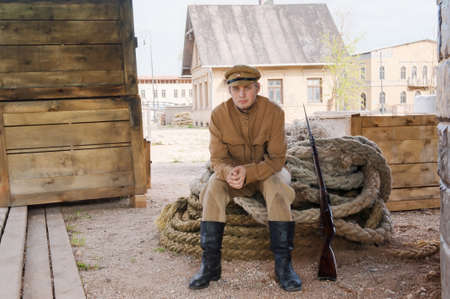 Soldier with a gun in uniform of World War I, sit down on the rope. Costume accord the times of...